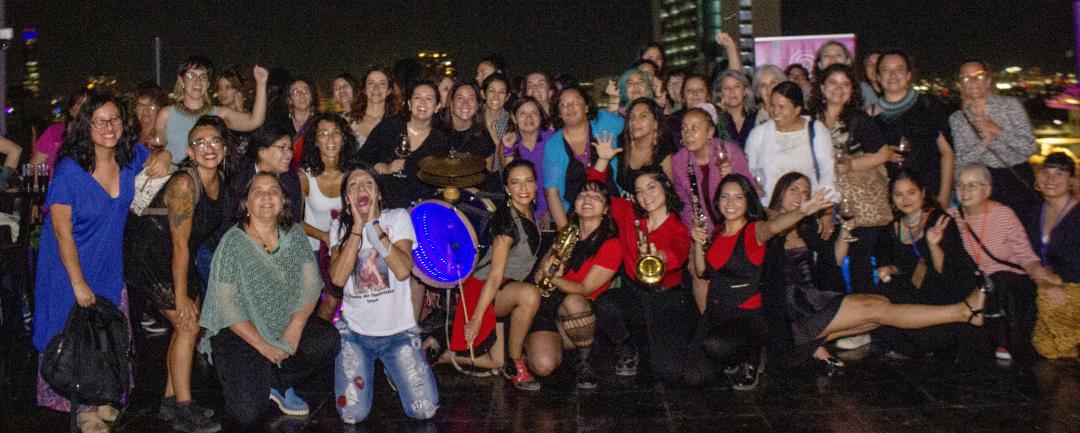 En la imagen se observan decenas de activistas posando sonrientes en la terraza de Galería CIMA. De fondo se distingue la Plaza Dignidad de noche.